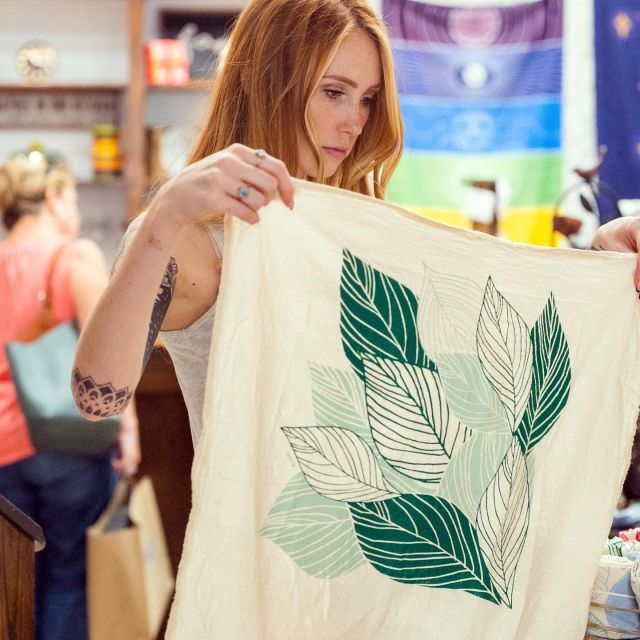 woman holding tea towel printed with leaf pattern at downtown Ashland gift shop