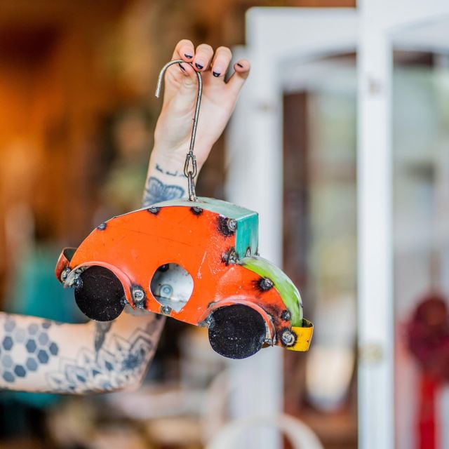 woman holds a hanging whimsical metal car art sculpture